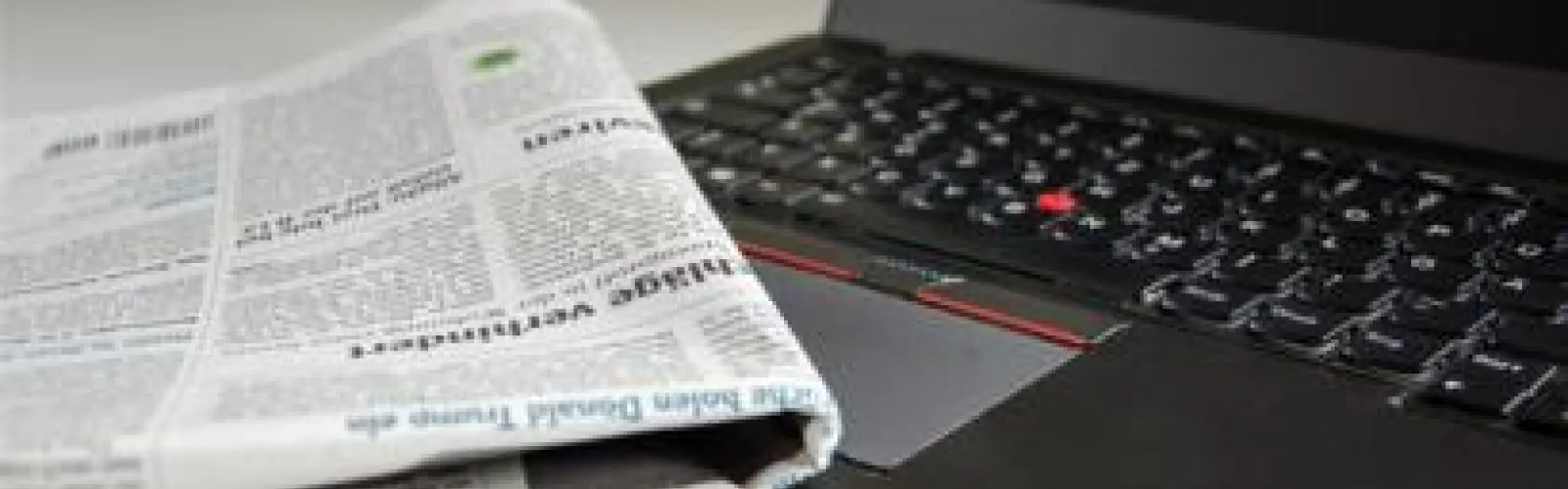 Newspaper lying beside a laptop.