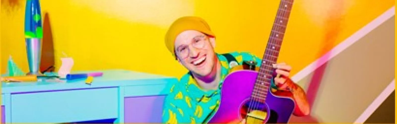 Man wearing a yellow beanie and a green shirt holding a purple guitar